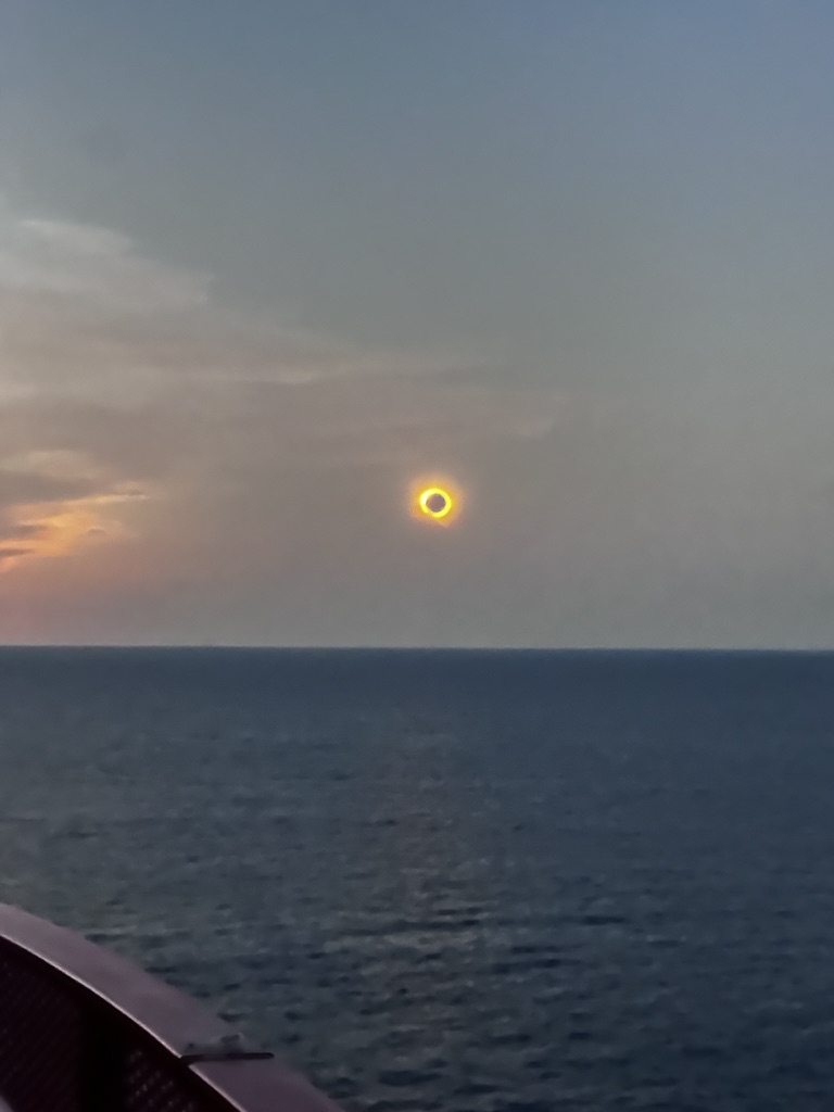 Total solar eclipse over the Mediterranean Sea photographed from a ship deck at dusk.